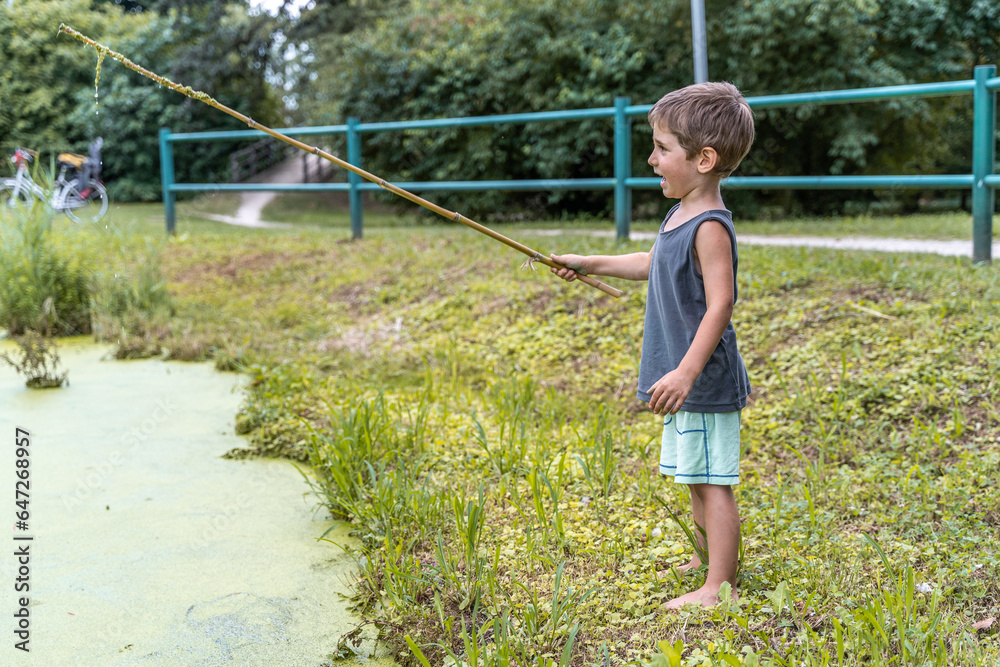 little smiling child playing with a stick by a pond in a public park little smiling child playing with a stick by a pond in a public park