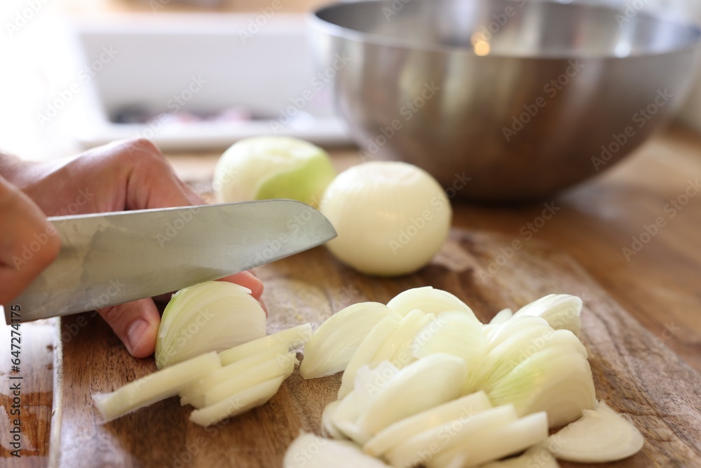 Woman cutting fresh ripe onion on wooden board, closeup