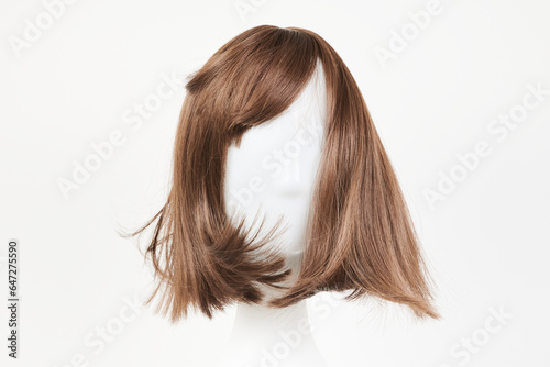 Natural looking dark brunet wig on white mannequin head. Middle length brown hair on the plastic wig holder isolated on white background, front view .