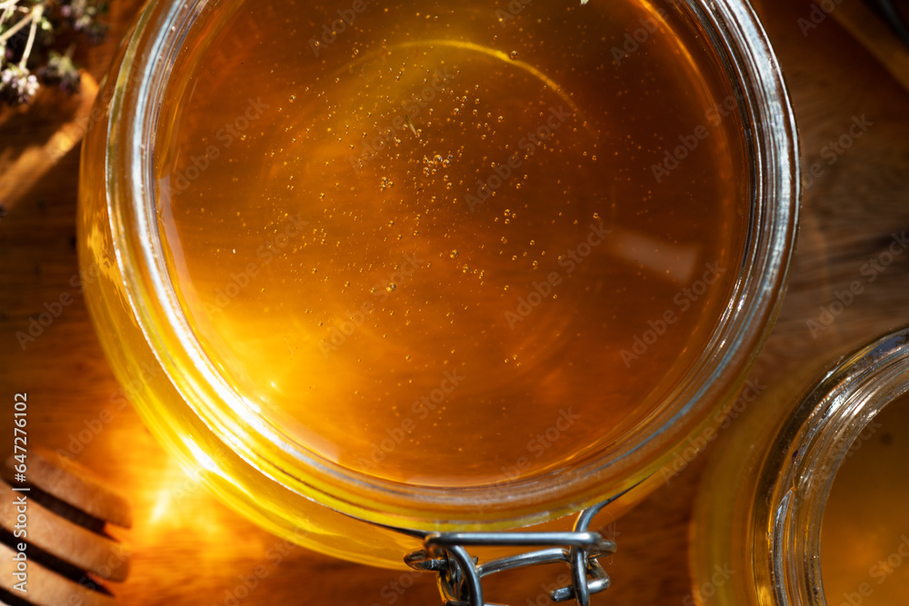 amazing fresh natural golden  linden honey in big glass jar  at wooden tray in beautiful sunny light. macro shot. top view