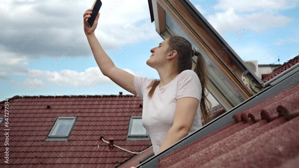 Young woman experiences signal issues with her cellphone as she peers out of an open attic window, attempting to regain a connection. Frustration of lost signal and connectivity problems. Young woman experiences signal issues with her cellphone as she peers out of an open attic window, attempting to regain a connection. Frustration of lost signal and connectivity problems.