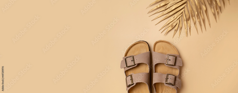 Trendy beige leather sandals, golden palm leaf on beige background, top view flat lay. Minimalistic concept of summer unisex fashionable shoes, flip-flop sandals for vacation, beach - obrazy, fototapety, plakaty 