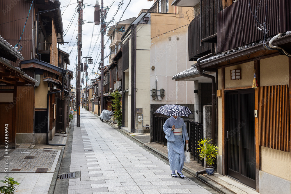 Unrecognizable woman in blue kimono walks with umbrella through a deserted street in Kyoto