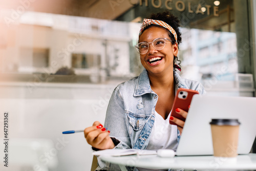 Photographie Happy female student sitting in a coffee shop, using a smartphone