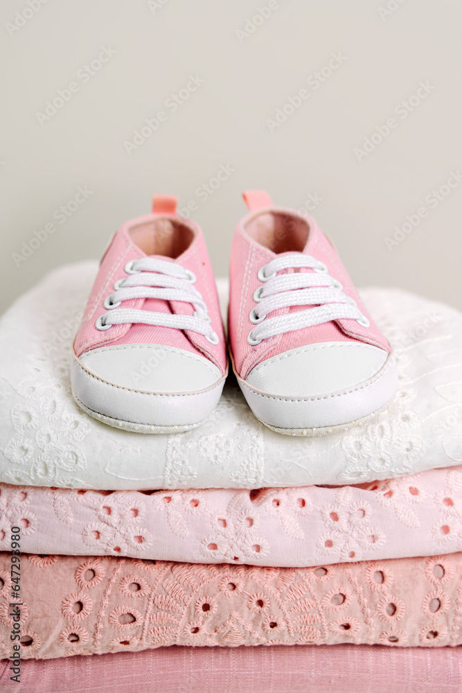 Stack of baby clothes with baby shoes. Cotton clothes and muslin swaddle blanket in pastel colors. Clean freshly laundered, neatly folded kids clothes. Close up Stack of baby clothes with baby shoes. Cotton clothes and muslin swaddle blanket in pastel colors. Clean freshly laundered, neatly folded kids clothes. Close up