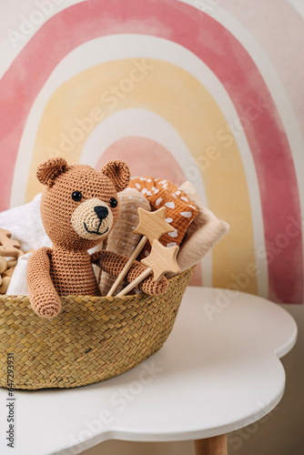 Basket with baby stuff and accessories for newborn. Gift basket with cotton clothes and muslin swaddle blanket, baby shoes, toys and cute teddy bear in beige colors.