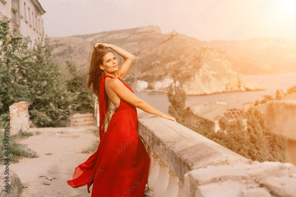 Woman red dress. Summer lifestyle of a happy woman posing near a fence with balusters over the sea. Woman red dress. Summer lifestyle of a happy woman posing near a fence with balusters over the sea.