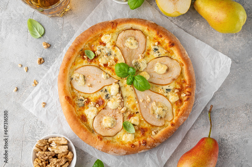 Delicious pizza with pears, gorgonzola cheese, walnuts and basil on a gray concrete background.