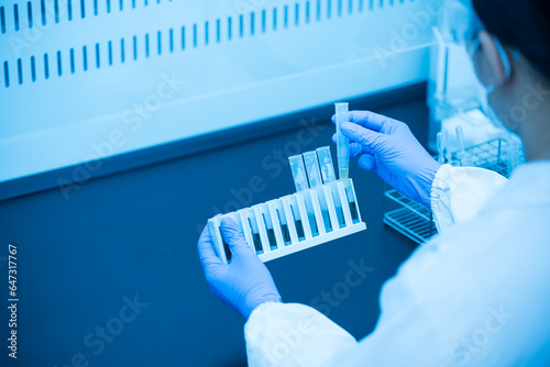 Close up scientist wearing blue gloves working with test tube in the flume hood at laboratory.Selective focus scientist hand holding sample blood test tube for fast laboratory at biochemistry unit.