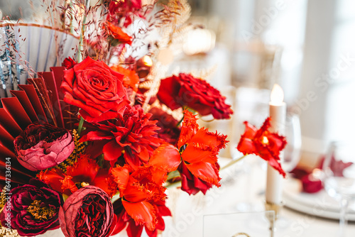 Red gold golden color decor, floral arrangement. Festive bouquet, table decoration. Traditional Chinese New Year party restaurant celebration. Roses,poppies,fan,candles,tassels.Chinese lunar calendar