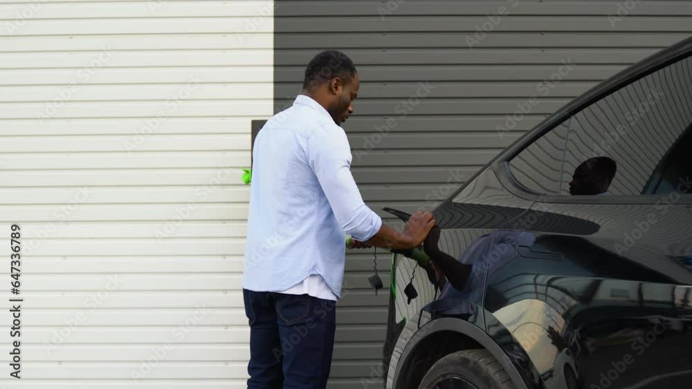 African american man disconnects power connector into luxury EV car at station African american man disconnects power connector into luxury EV car at station