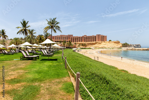 Sun loungers and umbrellas under palm trees on gorgeous beach on a sunny summer day. Omani Beach at the Barr Al Jissah Resort in Oman