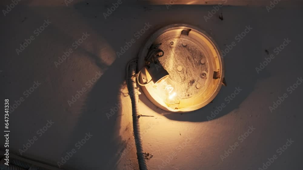 An incandescent light bulb glows in an old broken lamp on the concrete