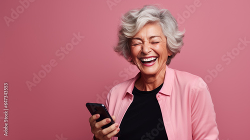 An elderly woman smiling and laughing with her phone against a colored background.