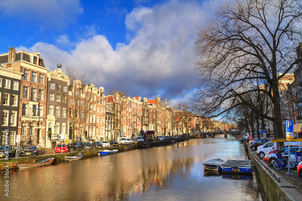 Cityscape on a sunny winter day - view of the houses and the city canal with boats in the historic center of Amsterdam, The Netherlands