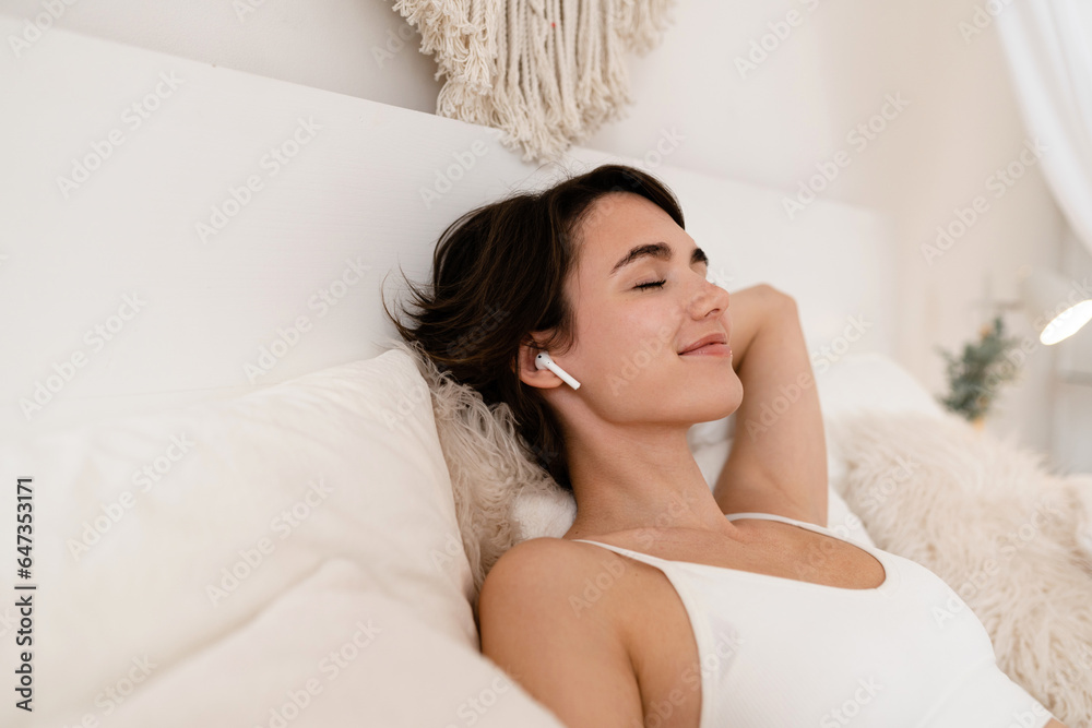 Naklejka premium woman wake up in morning in boho style bedroom, sitting on bed, listening to music, relaxing