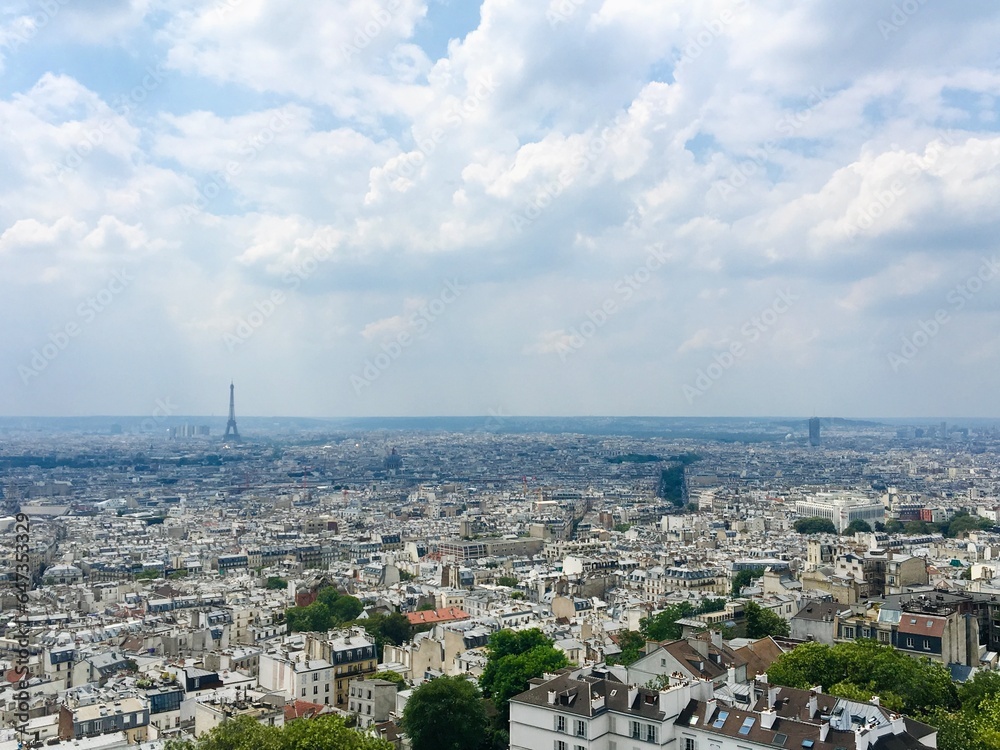 Overlooking all of Paris and the Eiffel Tower on a sunny Summer day with a fluffy white cloud filled sky