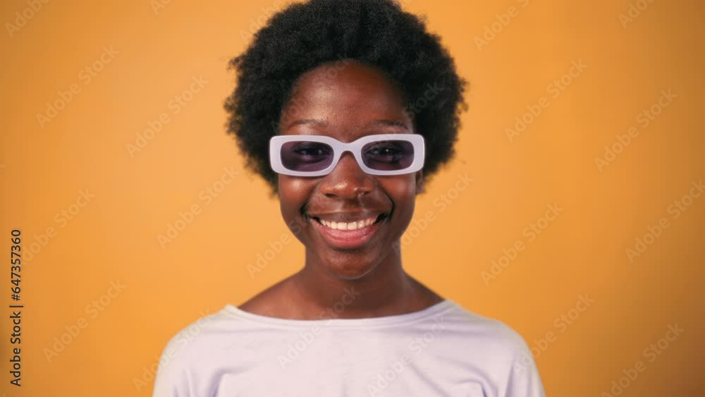 African American young woman with afro hair styling in glasses standing in sweater on a bright orange background and smiling. African American young woman with afro hair styling in glasses standing in sweater on a bright orange background and smiling.