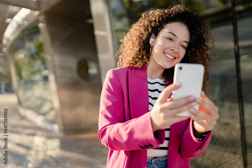 pretty curly woman in city street in stylish pink jacket, student education