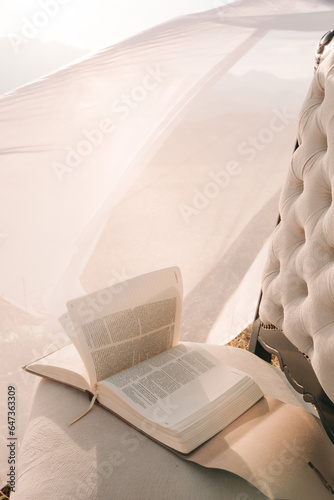 Bible on top of a chair in a shepherd with dry and yellowed grass. Winds leafing through the pages of the Bible book and white cloth swaying in the wind.