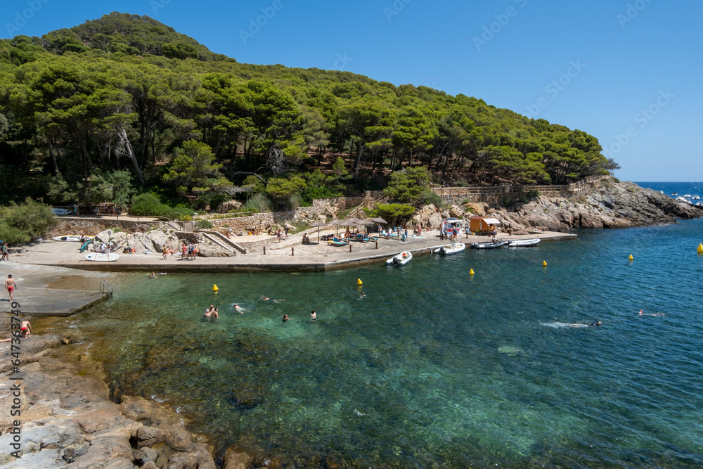 Image of a rocky beach in the Costa Brava with boats in the background.