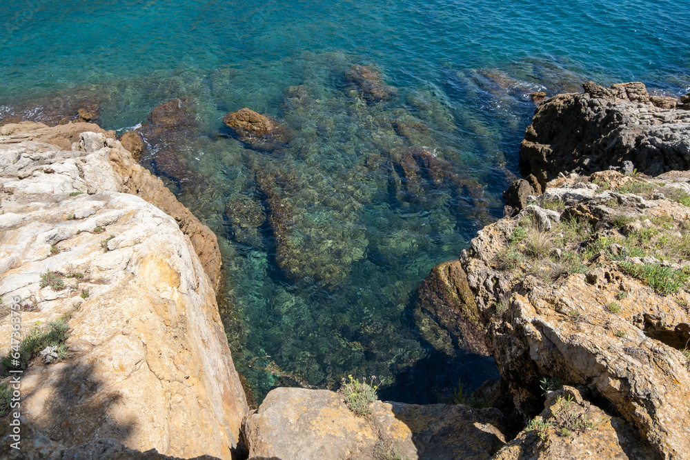 Image of the crystal-clear waters of the Mediterranean Sea in the Costa Brava, with the sun's reflection on its waves breaking against the rocks.