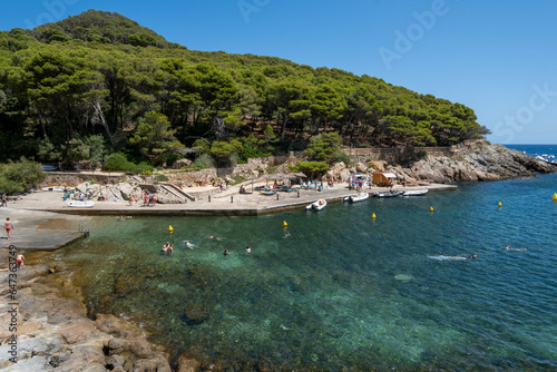Image of a rocky beach in the Costa Brava with boats in the background.