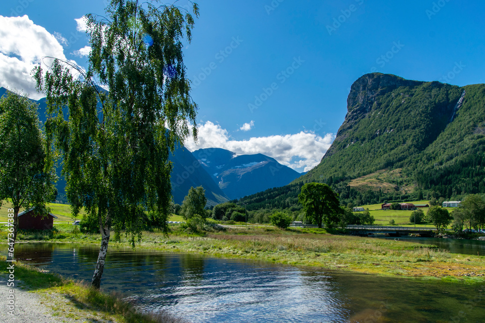 Norway, idyllic scene with a lake among mountains and a traditional red rorbu house on a green meadow.
