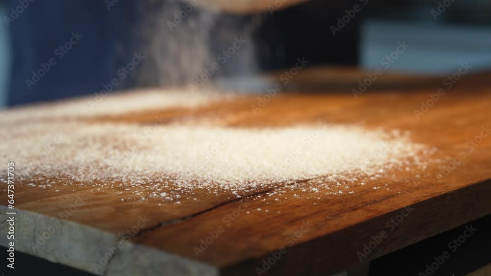 Wooden work surface with flour. Man's hand scatters flour through a sieve from above. Close-up.
