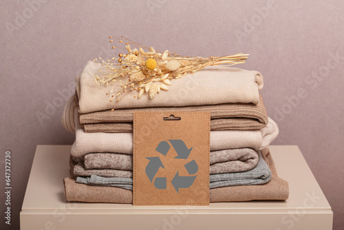 Stack of second hand clothes with used wardrobe for reuse and card with circular economy logo. Reusing, recycling materials and reducing waste in fashion, second hand apparel idea. Zero waste concept