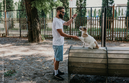 A young guy walks and trains his dogs Jack Russell terriers in a specially equipped dog walking area.