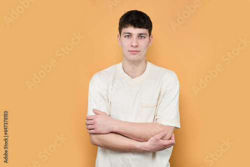 Portrait of a calm self-confident 18-year-old boy on a yellow background in white t-shirt, good support from family and friends give the boy strength and inspiration to move on and be successful