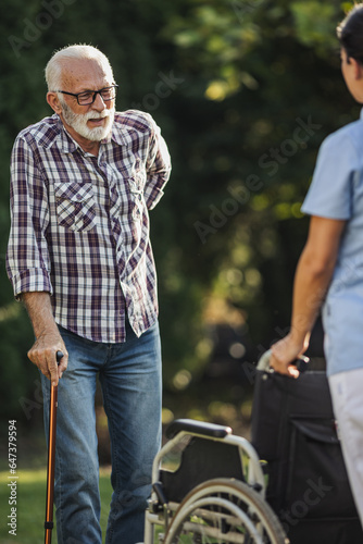 Senior man walking with stick toward wheelchair