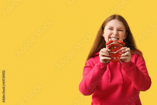 Stressed young woman with alarm clock on yellow background. Deadline concept