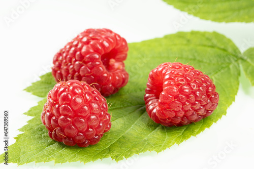 Three ripe raspberries lie on a green leaf. White background.