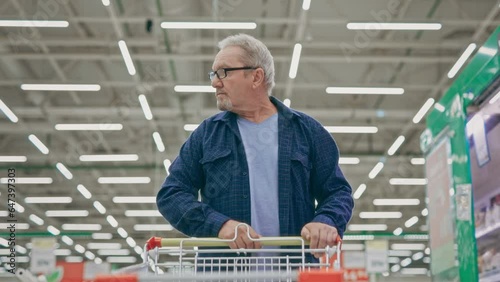 A senior man is walking through a supermarket with a trolley. Pensioner in a grocery shop