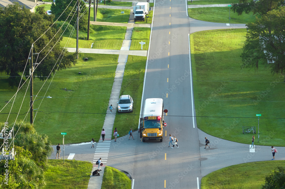 Aerial view of american yellow school bus picking up children at sidewalk bus stop for their lessongs in early morning. Public transportation in the USA