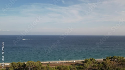 Aerial video shooting. A drone flies over the trees of Vaugrenier Park in Villeneuve-Loubet-Plage, France, approaching a road filled with cars and the Mediterranean Sea. photo