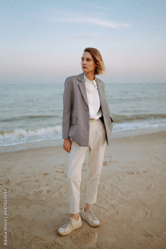 Stylish woman posing on autumn beach in wild grass. A woman enjoys the autumn nature on the beach, relaxing. Fashion, style and relaxation concept. Stylish woman posing on autumn beach in wild grass. A woman enjoys the autumn nature on the beach, relaxing. Fashion, style and relaxation concept.
