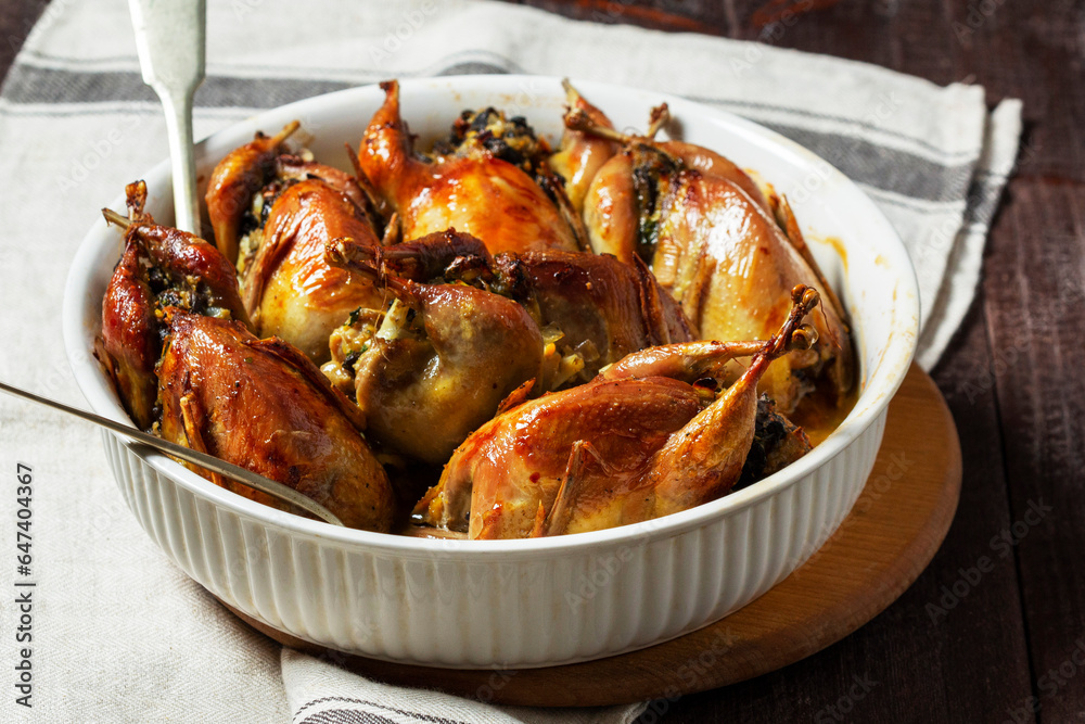 Baked quail stuffed with mushrooms, eggs and bread in a ceramic form on a wooden table.