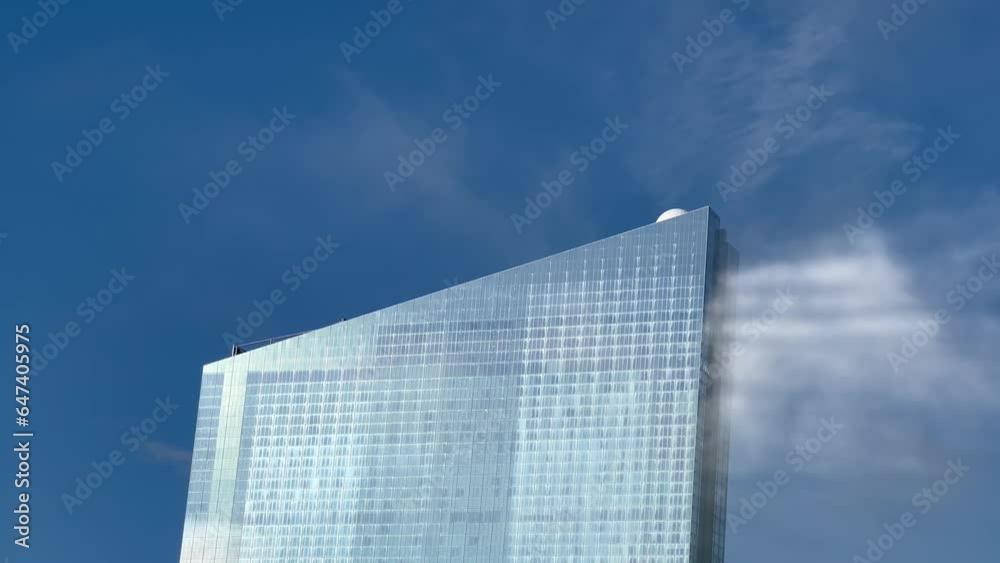 Mist and clouds are seen hitting the top of a glass building in a otherwise clear day with blue sky Mist and clouds are seen hitting the top of a glass building in a otherwise clear day with blue sky