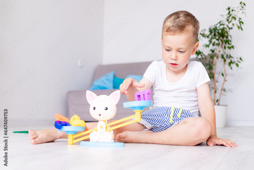 cute baby boy plays with scales at home on the floor trying to balance them, the concept of early development of children cute baby boy plays with scales at home on the floor trying to balance them, the concept of early development of children