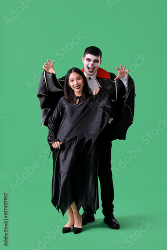 Young couple in costumes for Halloween party on green background