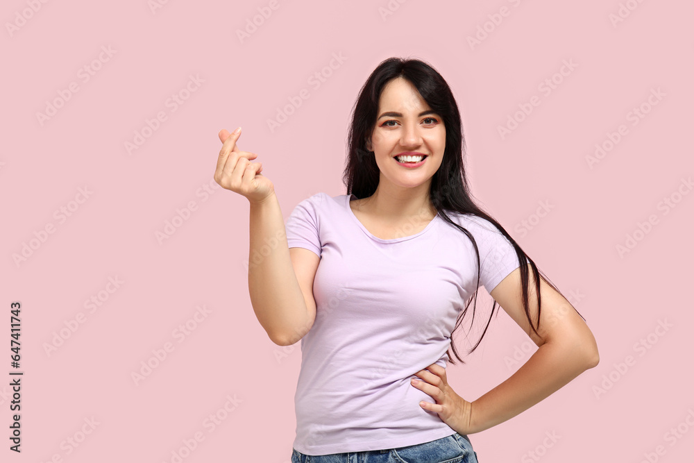 Happy young woman making heart with her fingers on pink background Happy young woman making heart with her fingers on pink background
