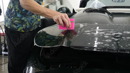 Close up of paint protection film installation on front bumper of modern luxury car. PPF is polyurethane film applied to car surface to protect the paint from stone chips, bug splatter, and abrasion.