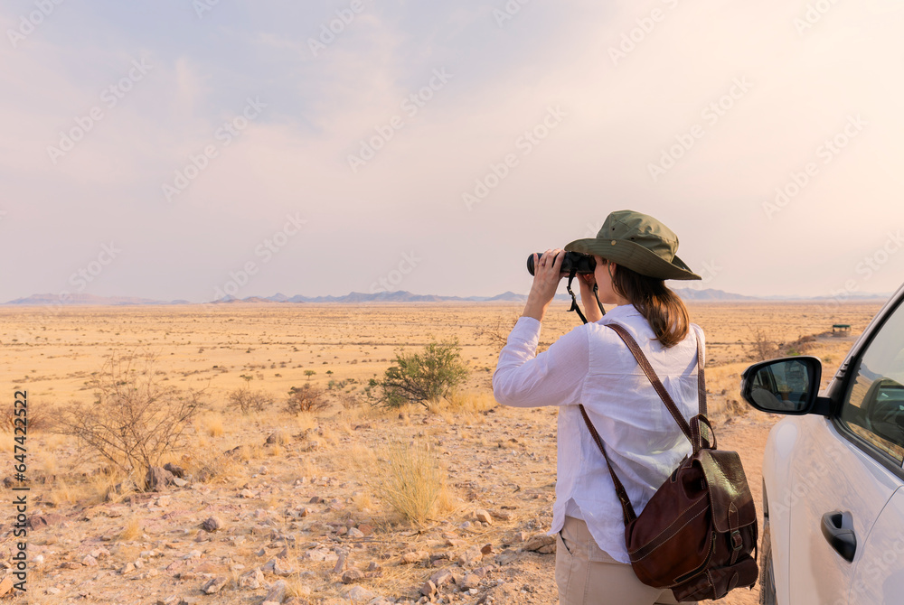 Obraz premium Woman with binoculars enjoying a beautiful view of the African savannah during a safari tour in Tanzania and Kenya. Adventure and wildlife exploration in Africa. Serengeti National Park.