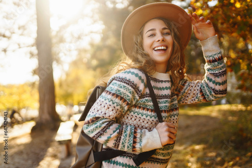 Beautiful woman in a stylish sweater and hat walks in the autumn forest, enjoys nature, feels freedom. Concept of nature, relaxation.