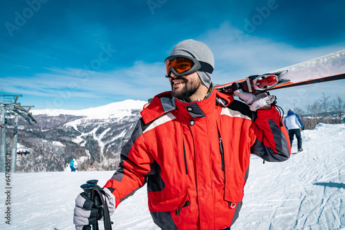 Konstfotografi Portrait of young male smiling skier standing on top of mountain while holding skies
