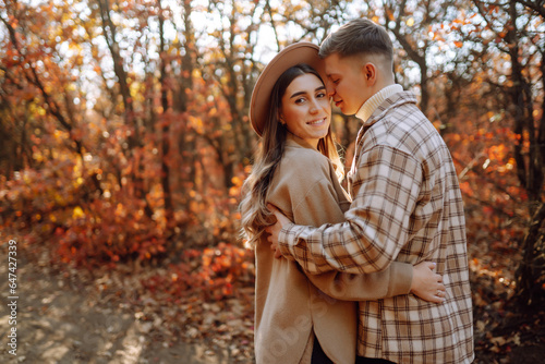 Young man and woman are walking, spending time together in the autumn forest. Beautiful couple enjoying nature outdoors in autumn. Concept for style, fashion, love or relaxation.