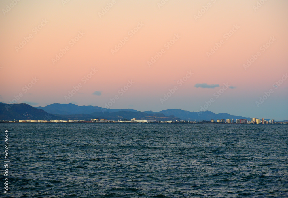 Coastline on sunset. Mediterranean sea at Alboraya beach and Port Saplaya in Valencia. Waves at sea on sunset. Seaside Spain beach on sunrise. Coastline in evening time. Shore on mountains landscape.